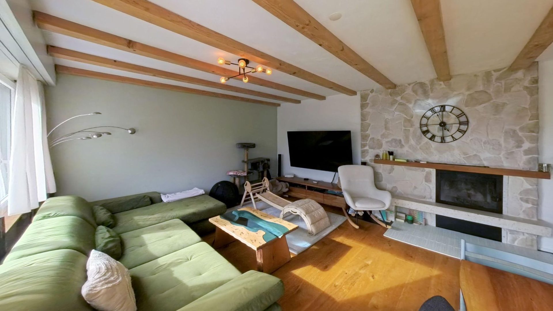 Wohnzimmer mit Cheminée in einer Natursteinwand und Balkendecke