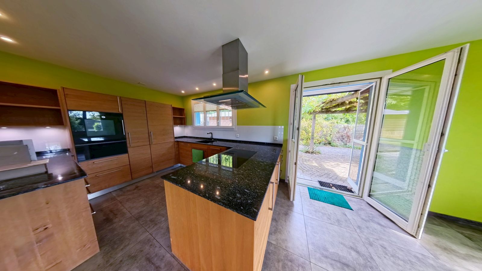 Küche mit Kochinsel, Holzfronten und offener Flügeltür zum Garten im Einfamilienhaus in Beringen SH, aufgenommen von RoomView360